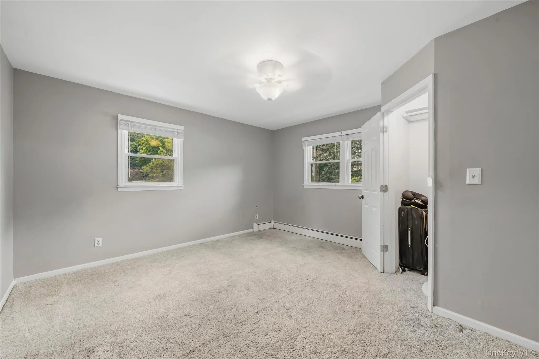 Light gray wall finishes with white trim, two windows, carpet flooring, ceiling-mounted light fixture, and an open closet Light gray wall finishes with white trim, two windows, carpet flooring, ceiling-mounted light fixture, and an open closet