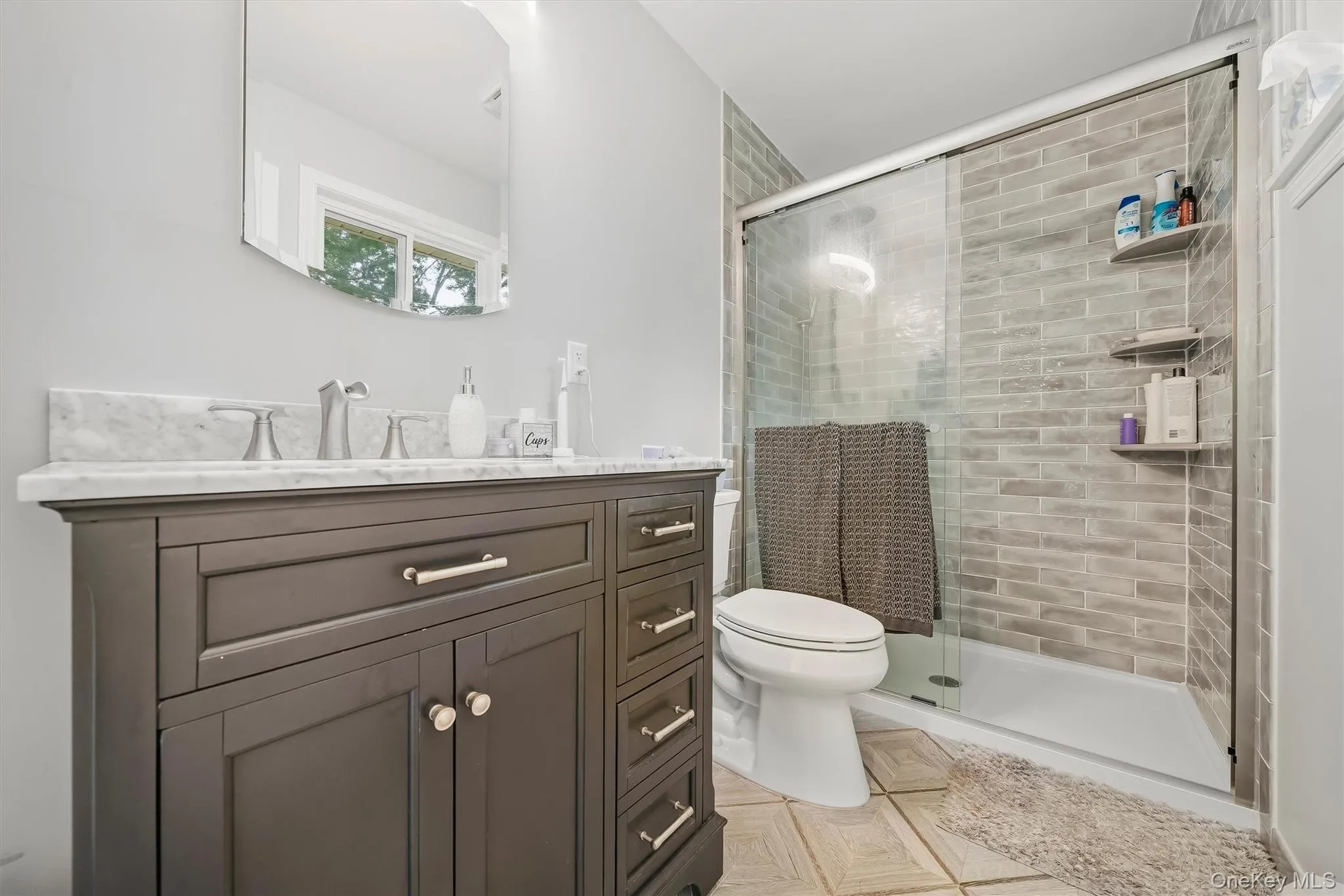 Dark wood vanity with a white marble countertop, brushed nickel faucet, and an arched frameless mirror Dark wood vanity with a white marble countertop, brushed nickel faucet, and an arched frameless mirror