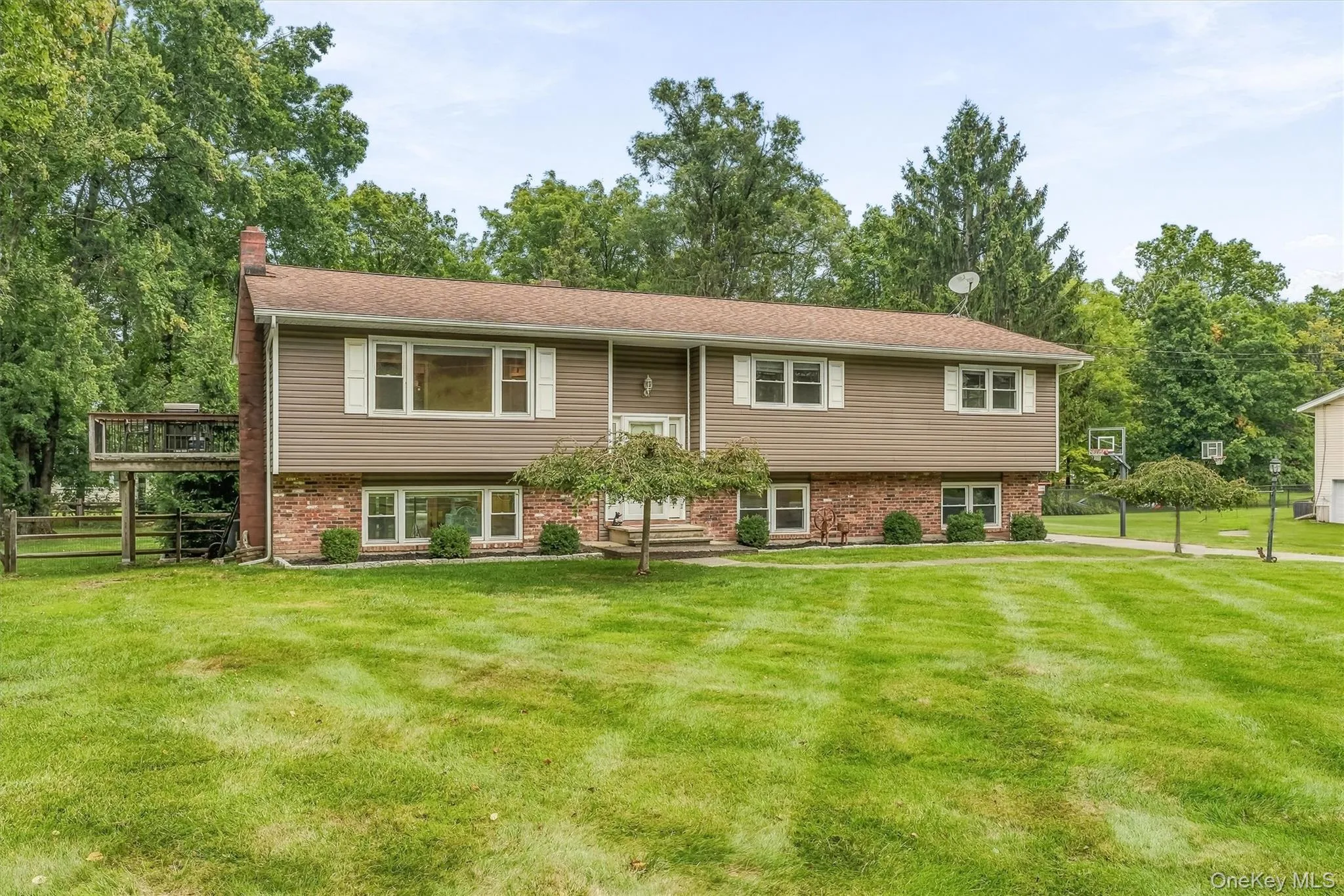 Two-story residence featuring composite siding, brick façade, multiple windows with shutters, an elevated outdoor deck, and established lawn with mature trees Two-story residence featuring composite siding, brick façade, multiple windows with shutters, an elevated outdoor deck, and established lawn with mature trees