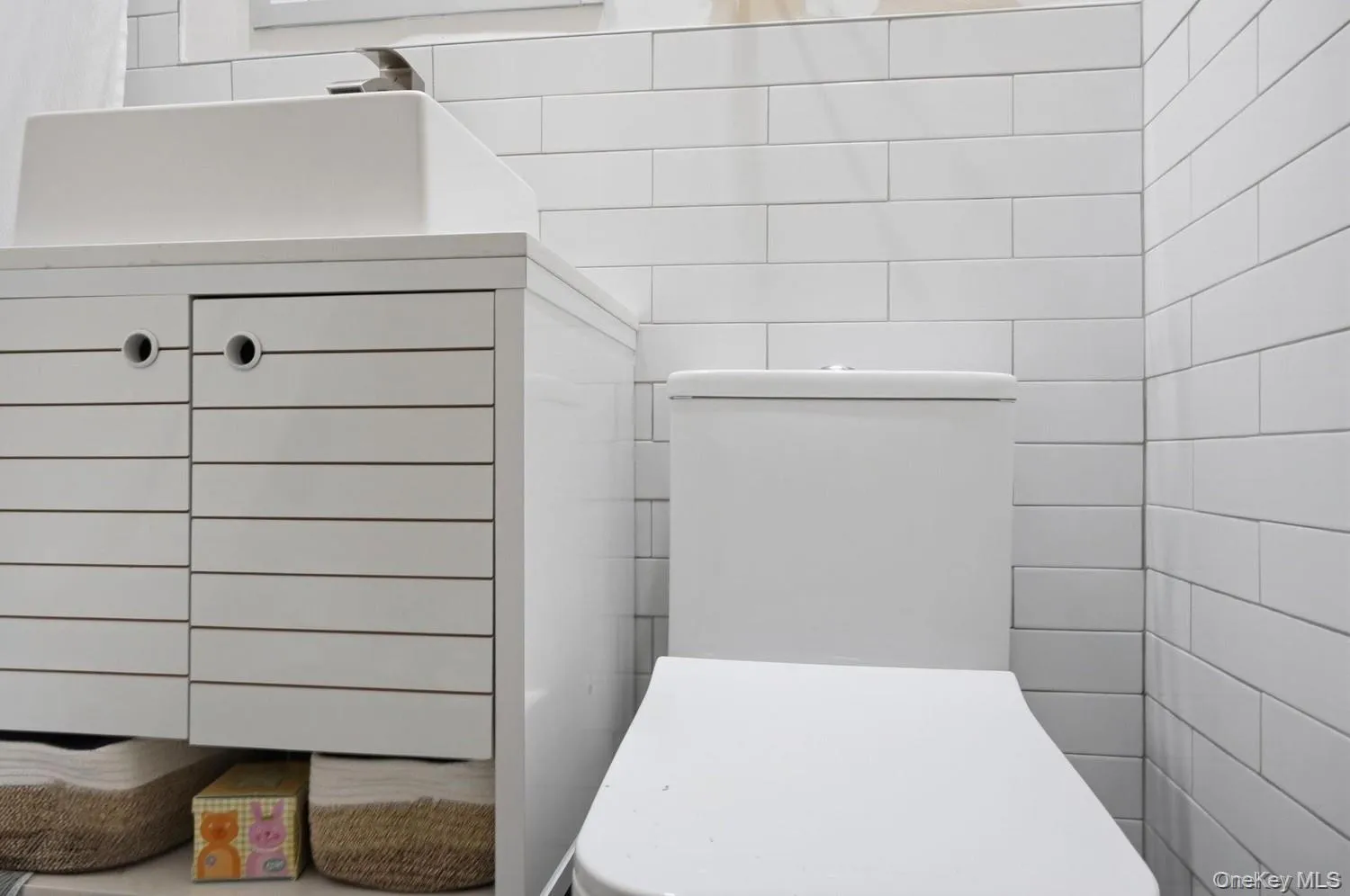 Modern bathroom featuring subway tile wall treatment, a contemporary white toilet with integrated tank, and horizontal shiplap cabinetry with brushed metal hardware Modern bathroom featuring subway tile wall treatment, a contemporary white toilet with integrated tank, and horizontal shiplap cabinetry with brushed metal hardware