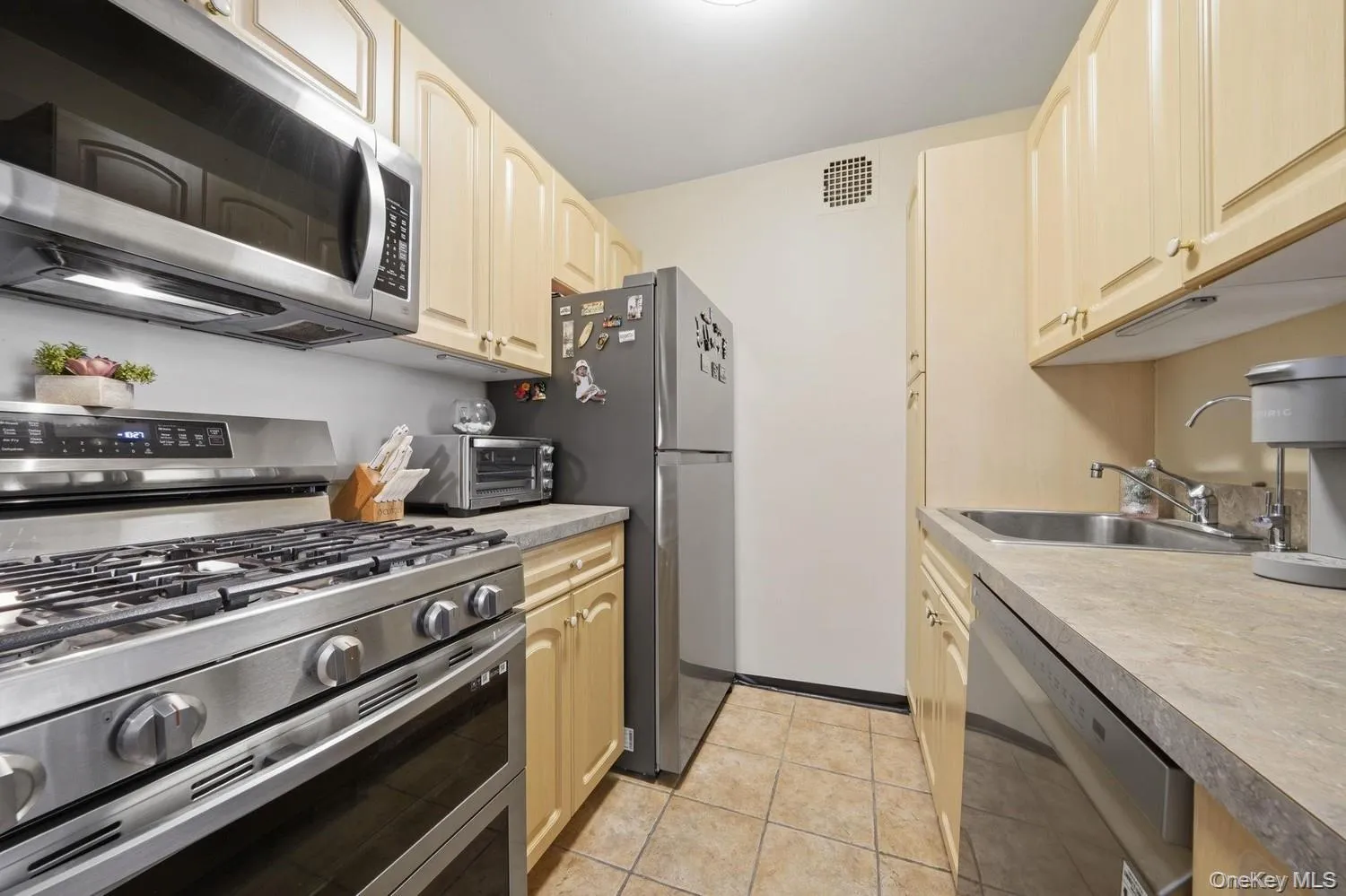 Kitchen featuring stainless steel appliances, light-toned cabinetry, light-toned countertops, and tiled flooring Kitchen featuring stainless steel appliances, light-toned cabinetry, light-toned countertops, and tiled flooring