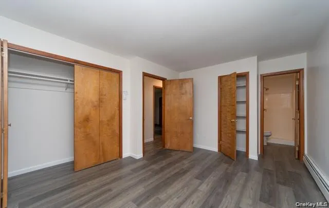 Wood-finish flooring, two wood-paneled closets with sliding doors, additional built-in shelving, and white baseboard heating Wood-finish flooring, two wood-paneled closets with sliding doors, additional built-in shelving, and white baseboard heating