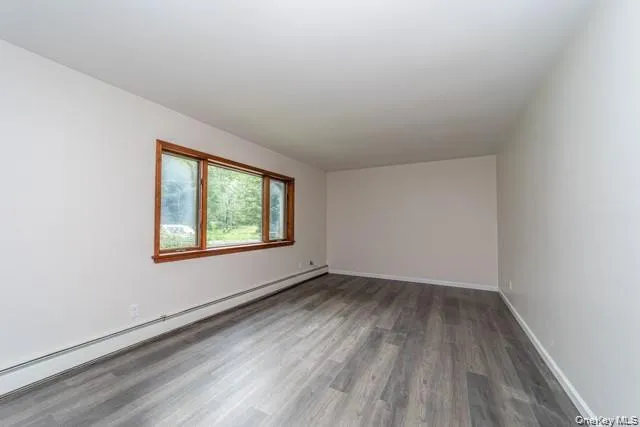 Spacious room featuring wood-finish flooring, a large multi-pane window with wood trim, and light-colored walls Spacious room featuring wood-finish flooring, a large multi-pane window with wood trim, and light-colored walls