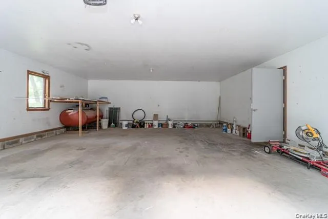 Spacious garage featuring concrete flooring, white painted walls, a window with wood trim, and a utility door Spacious garage featuring concrete flooring, white painted walls, a window with wood trim, and a utility door
