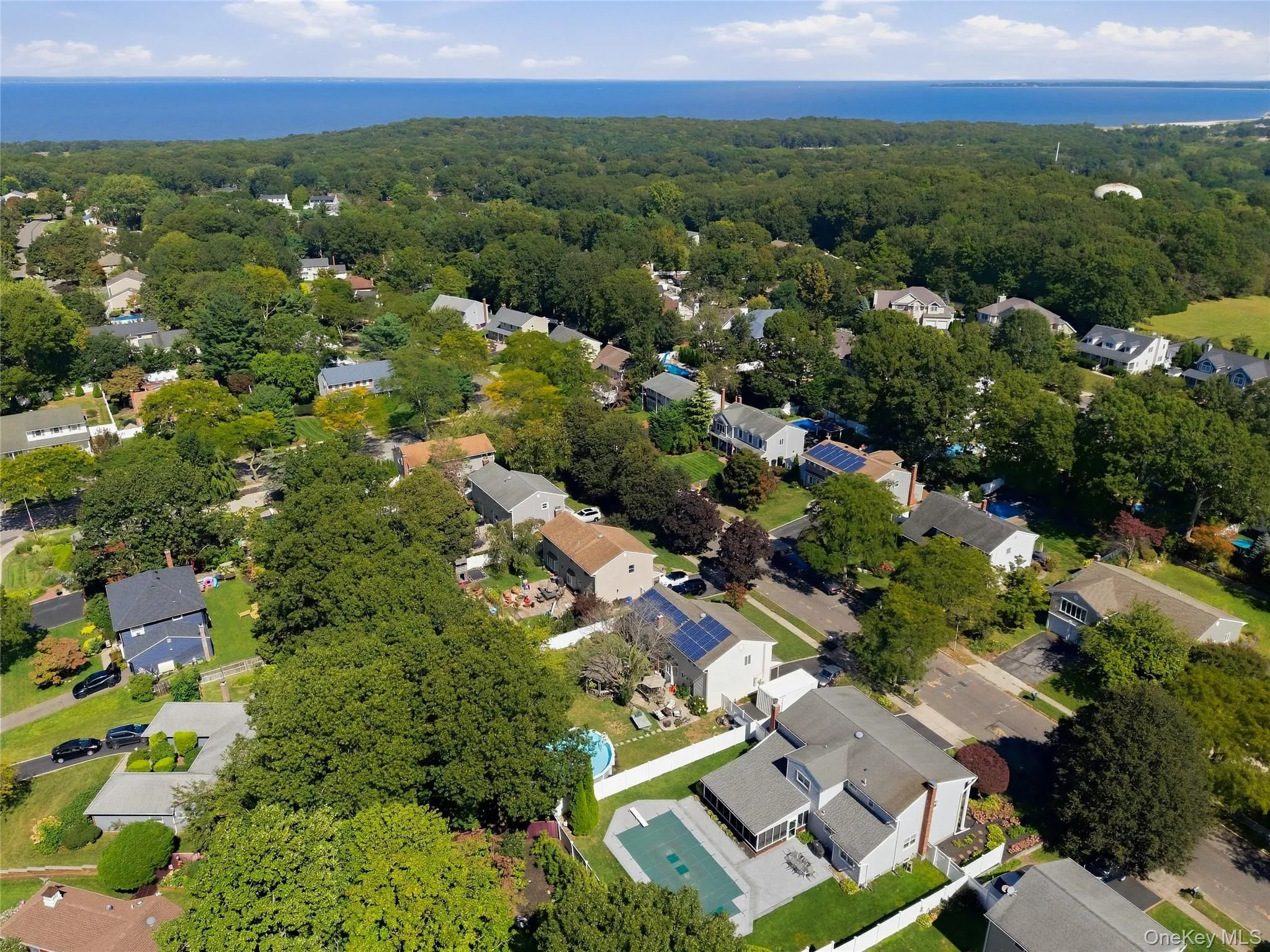 Residential neighborhood featuring mature trees, a community of single-family homes, and distant water scenery Residential neighborhood featuring mature trees, a community of single-family homes, and distant water scenery