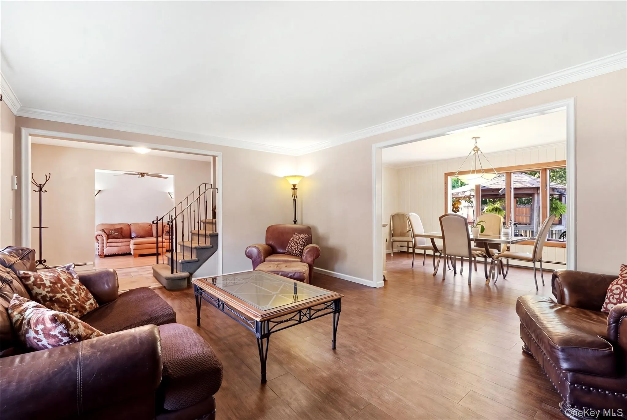 Hardwood-style flooring throughout, crown molding, and a staircase with an ornamental metal railing with view into dining room Hardwood-style flooring throughout, crown molding, and a staircase with an ornamental metal railing with view into dining room