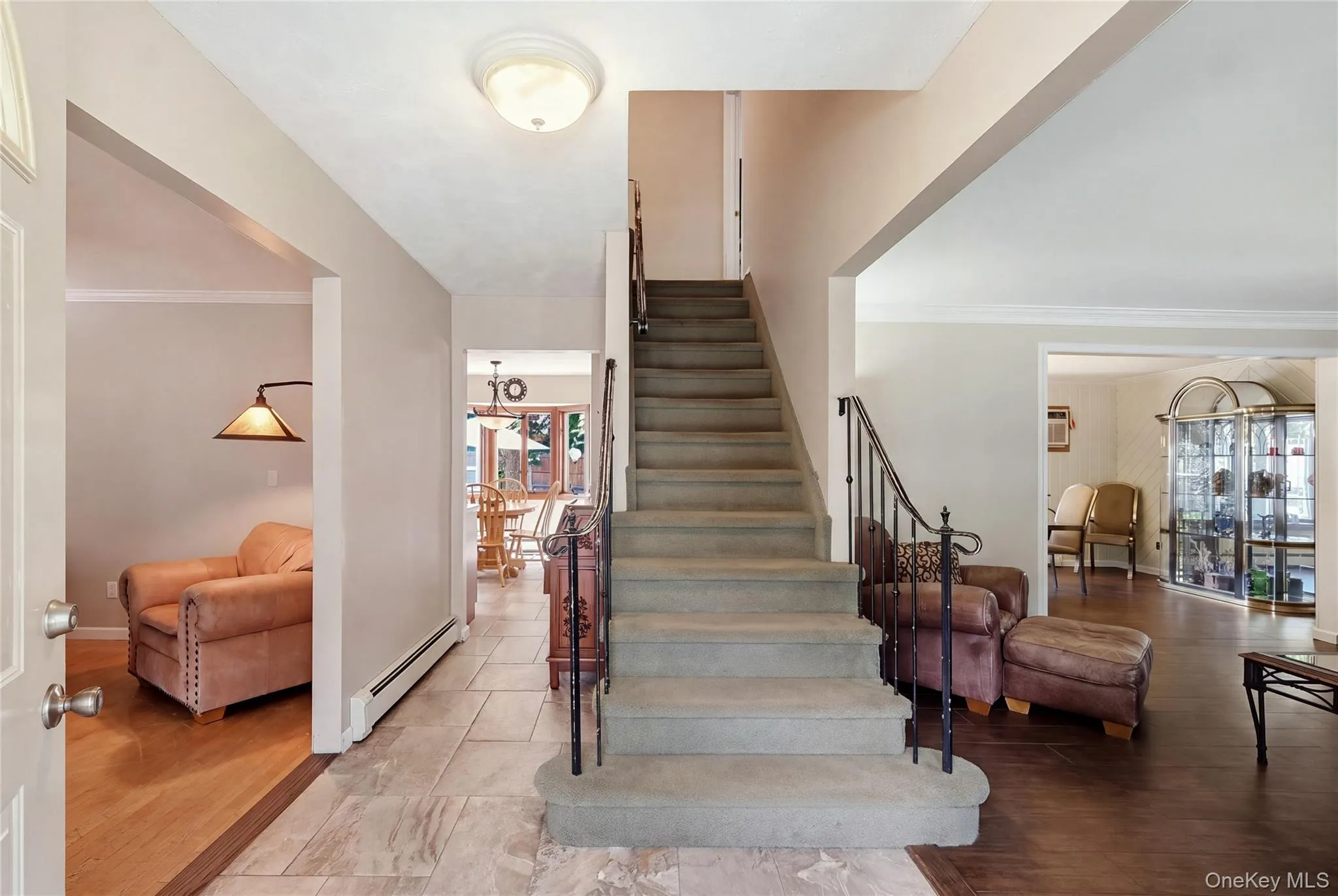 Foyer with tile flooring, a carpeted staircase with wrought iron railing, with view of kitchen, living room and den Foyer with tile flooring, a carpeted staircase with wrought iron railing, with view of kitchen, living room and den