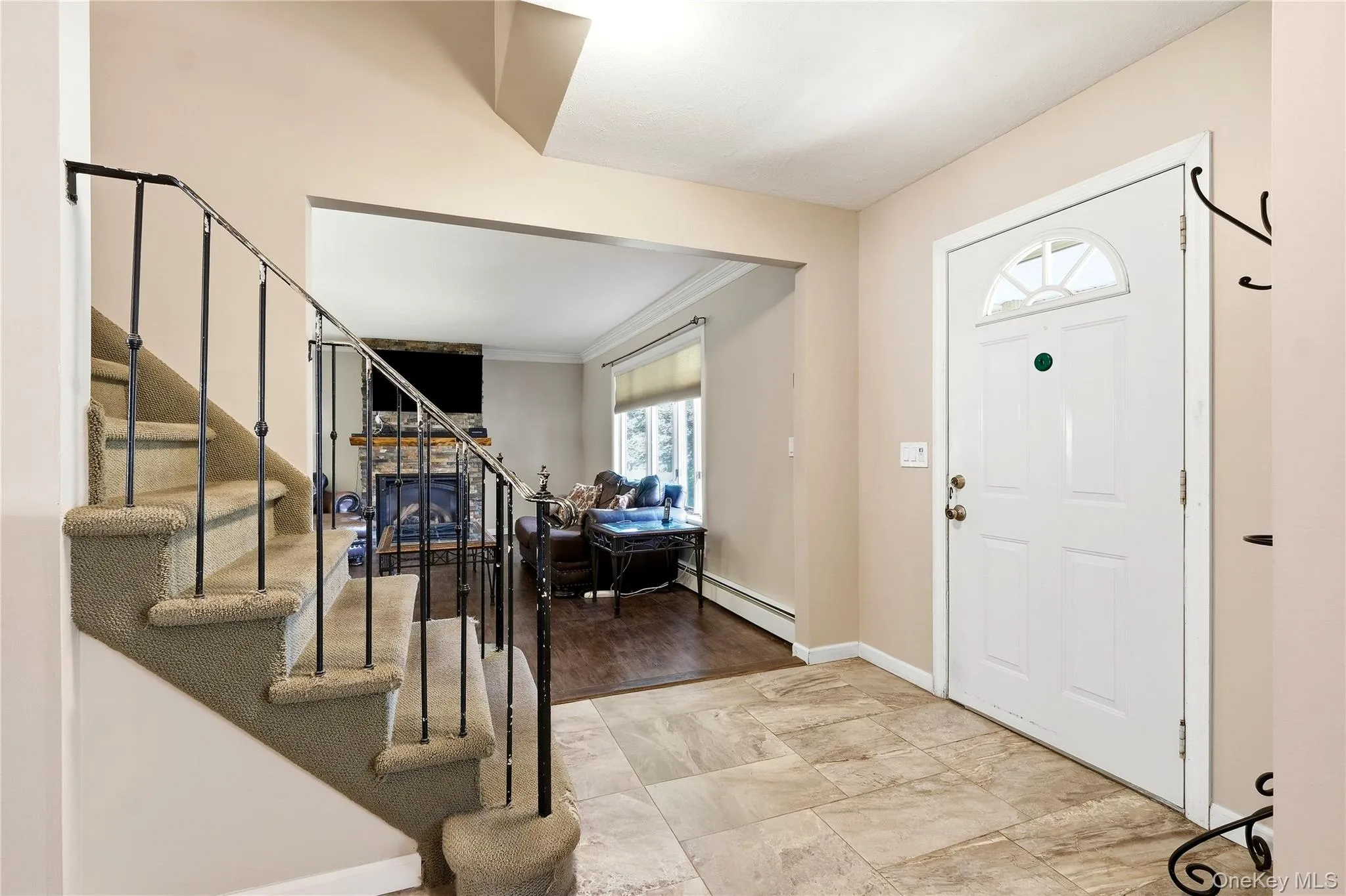 Entryway with tile flooring, a white paneled door with an arched transom, and a carpeted staircase with wrought iron railing with view into living room Entryway with tile flooring, a white paneled door with an arched transom, and a carpeted staircase with wrought iron railing with view into living room