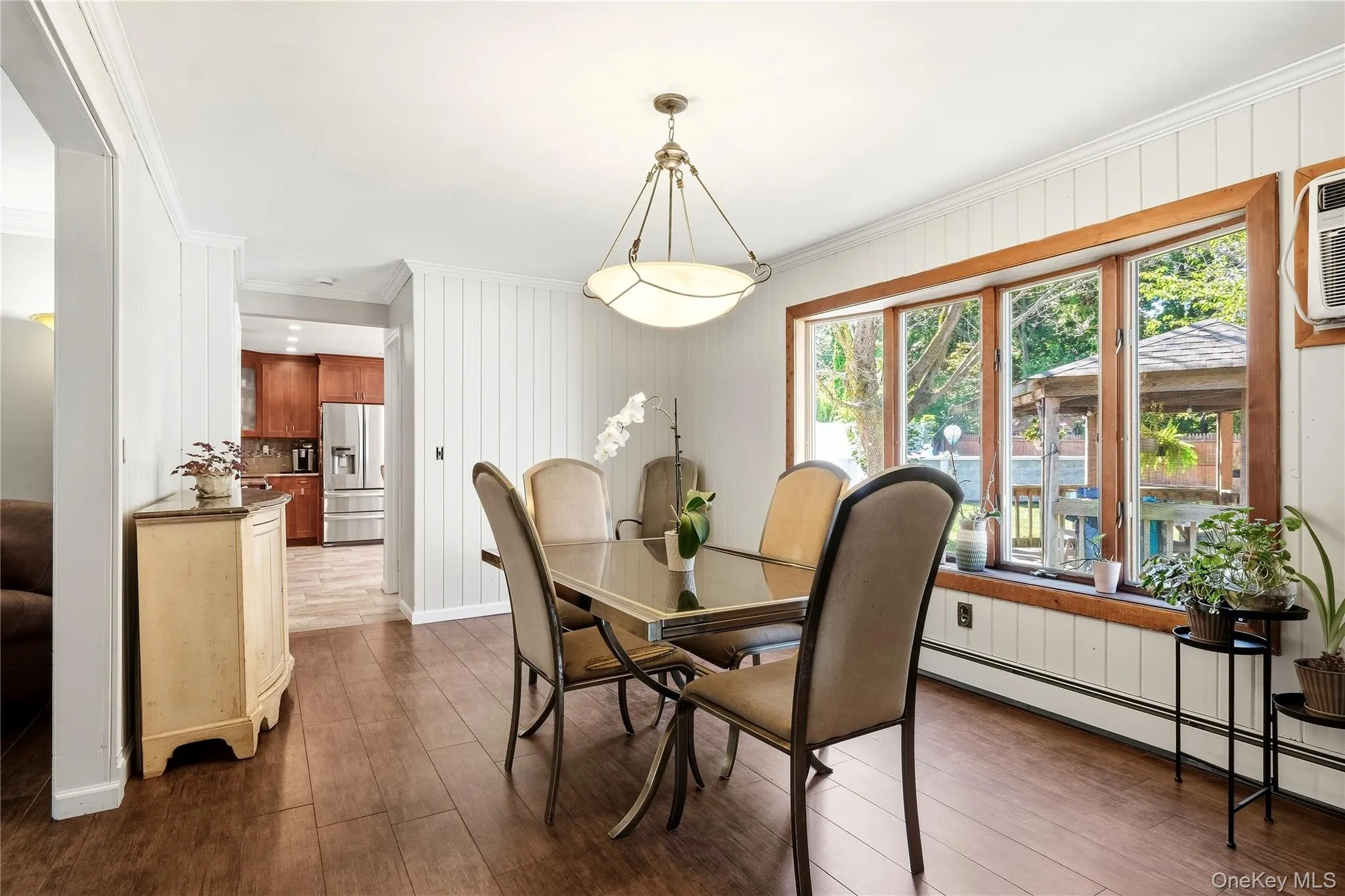 Oversized dining room featuring wood-finish flooring, a multi-pane window, white vertical paneling, and a contemporary ceiling light fixture Oversized dining room featuring wood-finish flooring, a multi-pane window, white vertical paneling, and a contemporary ceiling light fixture