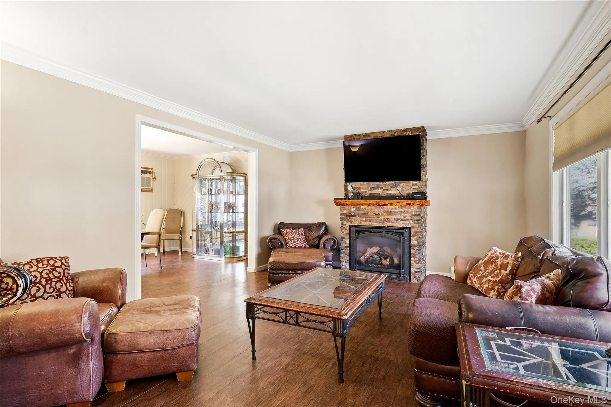 Living area featuring wood-finish flooring, a stone-clad gas fireplace with a wood mantle, and crown molding Living area featuring wood-finish flooring, a stone-clad gas fireplace with a wood mantle, and crown molding