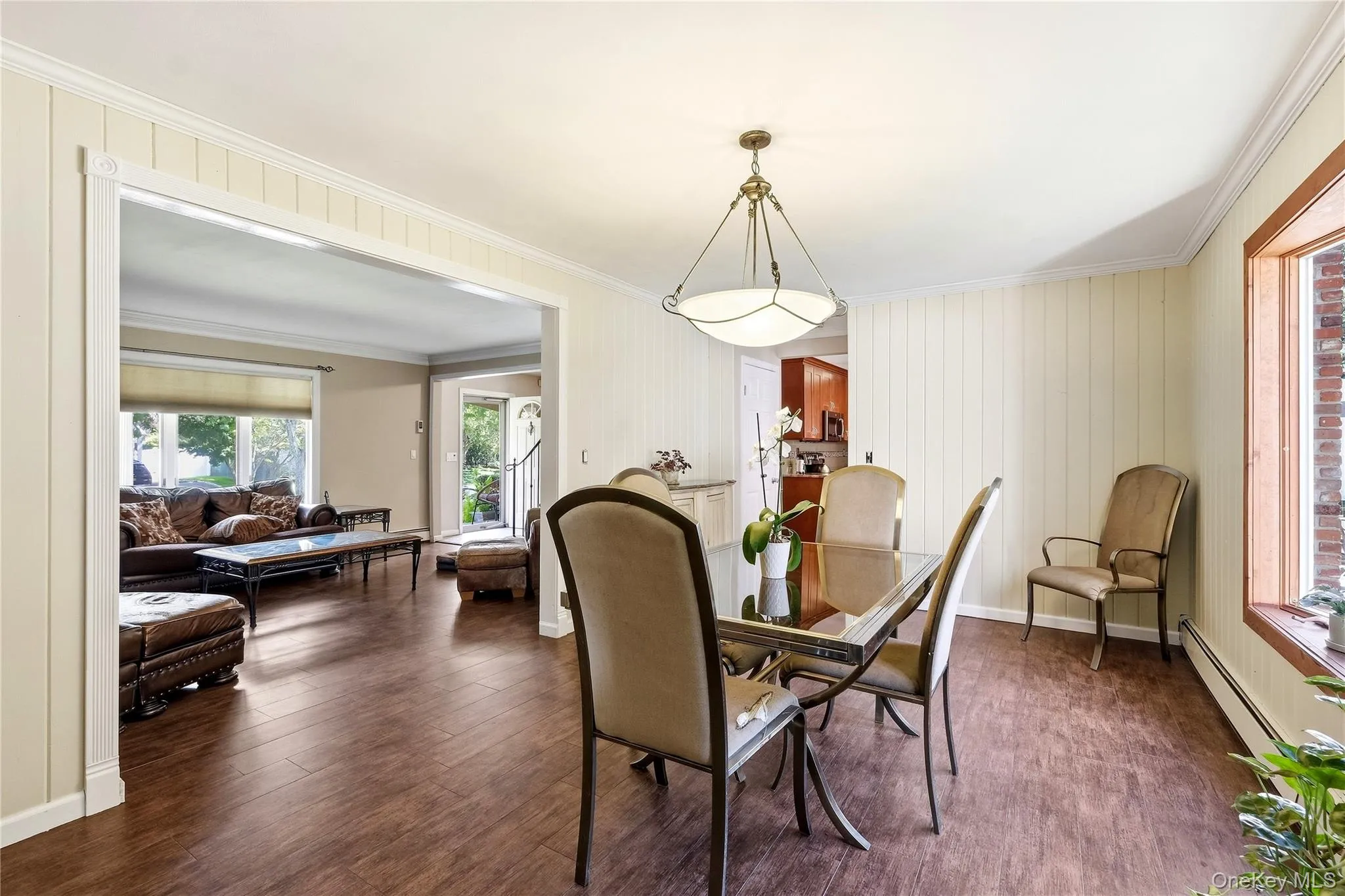 Oversized dining room featuring wood-finish flooring, a multi-pane window, white vertical paneling, and a contemporary ceiling light fixture Oversized dining room featuring wood-finish flooring, a multi-pane window, white vertical paneling, and a contemporary ceiling light fixture