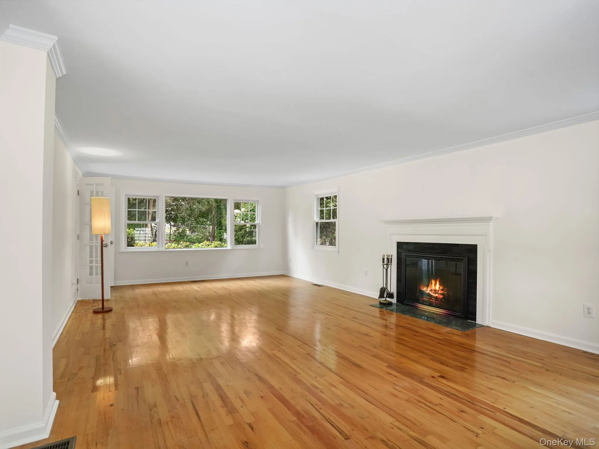 Unfurnished living room featuring light wood finished floors, ornamental molding, plenty of natural light, and a fireplace with flush hearth Unfurnished living room featuring light wood finished floors, ornamental molding, plenty of natural light, and a fireplace with flush hearth