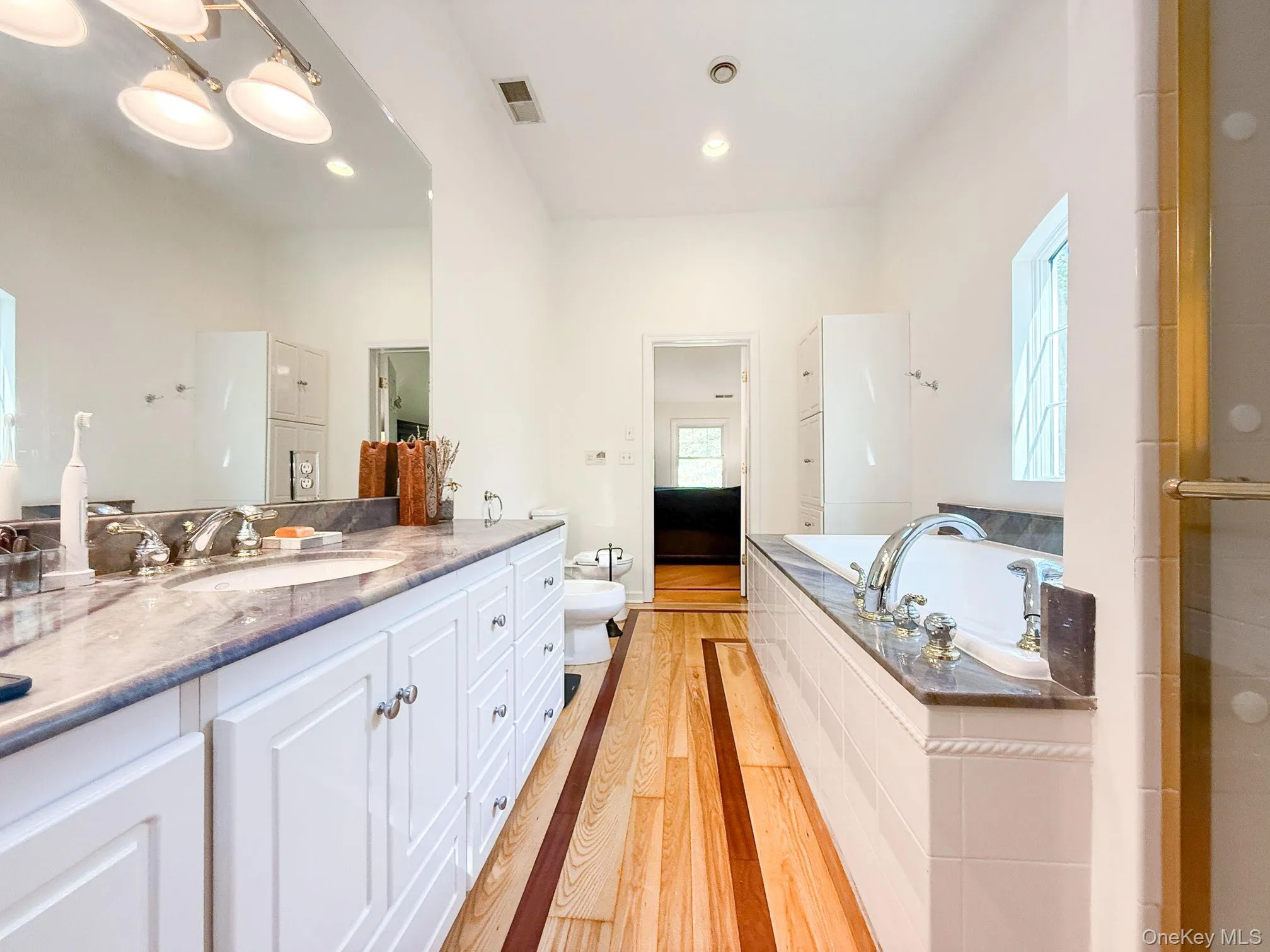 Full bathroom with vanity, a garden tub, a bidet, light wood-type flooring, and recessed lighting Full bathroom with vanity, a garden tub, a bidet, light wood-type flooring, and recessed lighting