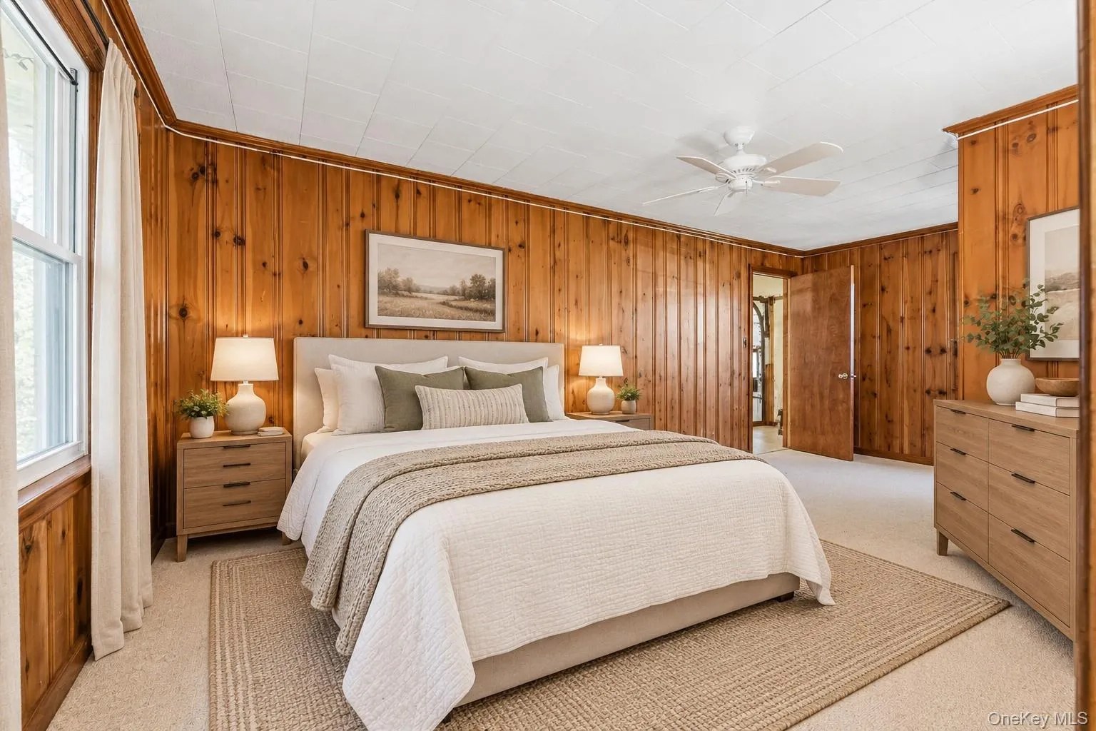 **Virtually Staged** Wood-paneled walls with light-colored carpeting, featuring a ceiling fan and a window with white trim **Virtually Staged** Wood-paneled walls with light-colored carpeting, featuring a ceiling fan and a window with white trim