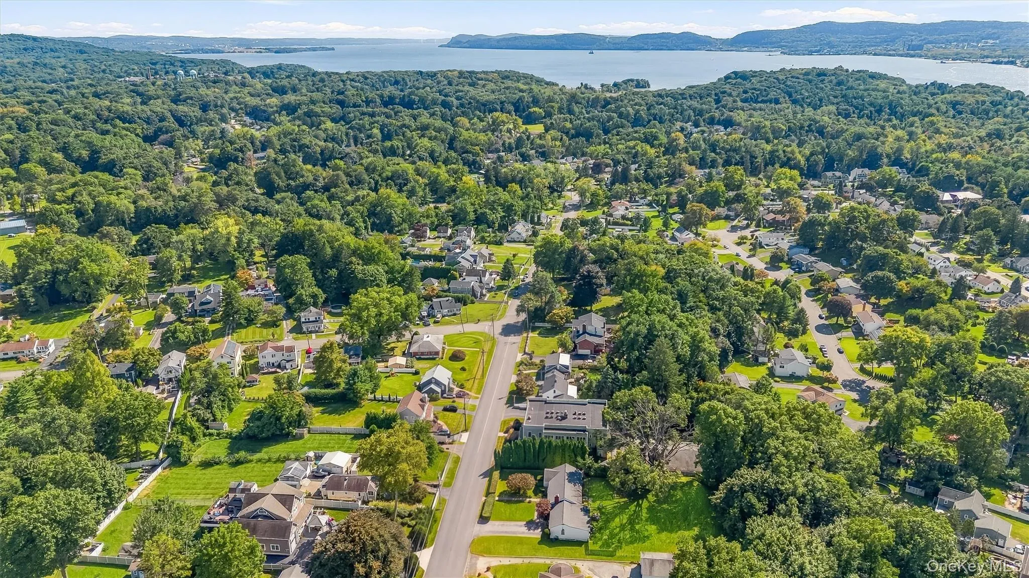 Aerial view showcasing a tree-lined residential community with mature landscaping, spacious home lots, and a serene waterfront backdrop Aerial view showcasing a tree-lined residential community with mature landscaping, spacious home lots, and a serene waterfront backdrop
