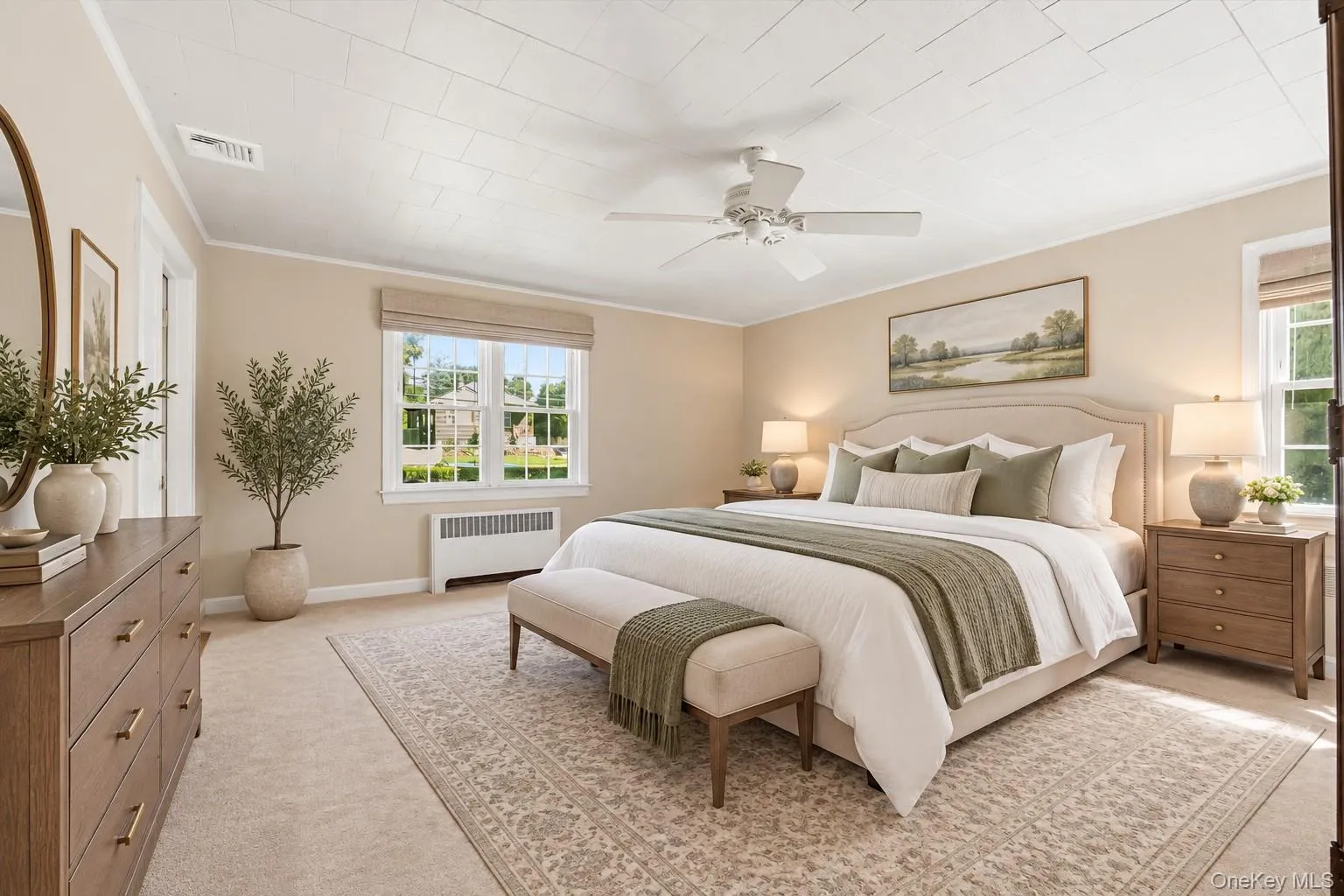 **Virtually Staged** Primary bedroom suite featuring a ceiling fan, dual nightstands with task lighting, wood-finish dresser with mirror, multiple windows with natural light, and neutral wall finishes complemented by coordinating area rug and window treatments **Virtually Staged** Primary bedroom suite featuring a ceiling fan, dual nightstands with task lighting, wood-finish dresser with mirror, multiple windows with natural light, and neutral wall finishes complemented by coordinating area rug and window treatments