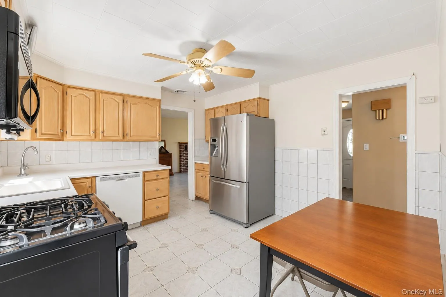 **Virtually Staged** Kitchen featuring wood-finish cabinetry, stainless steel refrigerator, white tile backsplash, and a ceiling fan with integrated lighting **Virtually Staged** Kitchen featuring wood-finish cabinetry, stainless steel refrigerator, white tile backsplash, and a ceiling fan with integrated lighting