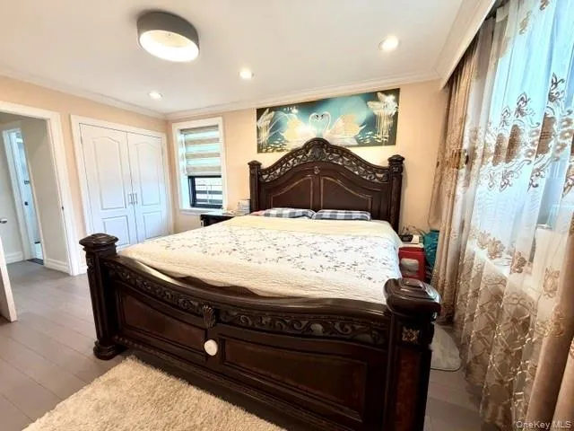 Recessed ceiling lighting, crown molding, wood-finish flooring, built-in closet with panel doors, and window with privacy blinds Recessed ceiling lighting, crown molding, wood-finish flooring, built-in closet with panel doors, and window with privacy blinds