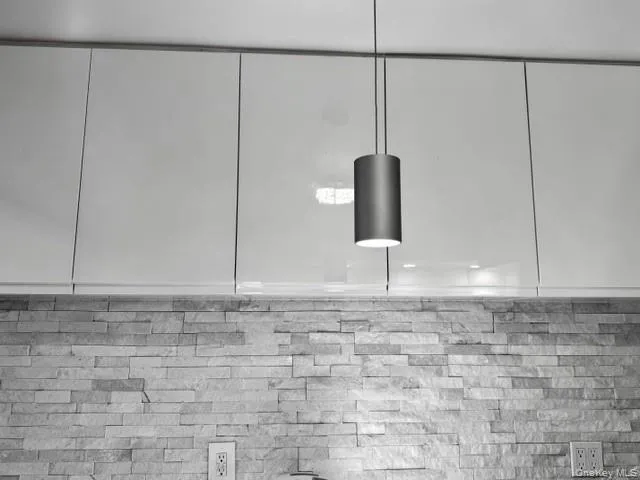 White glossy cabinetry with integrated handles, stacked stone backsplash, and recessed overhead lighting White glossy cabinetry with integrated handles, stacked stone backsplash, and recessed overhead lighting