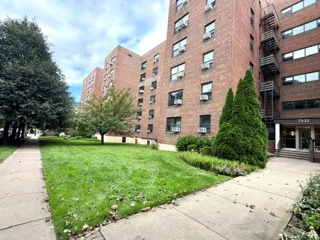 Brick facade building with multiple levels, featuring a concrete walkway and mature landscaping Brick facade building with multiple levels, featuring a concrete walkway and mature landscaping