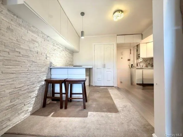 White stacked stone accent wall, upper white cabinetry, light wood-finish flooring, and a flush-mount ceiling light fixture White stacked stone accent wall, upper white cabinetry, light wood-finish flooring, and a flush-mount ceiling light fixture