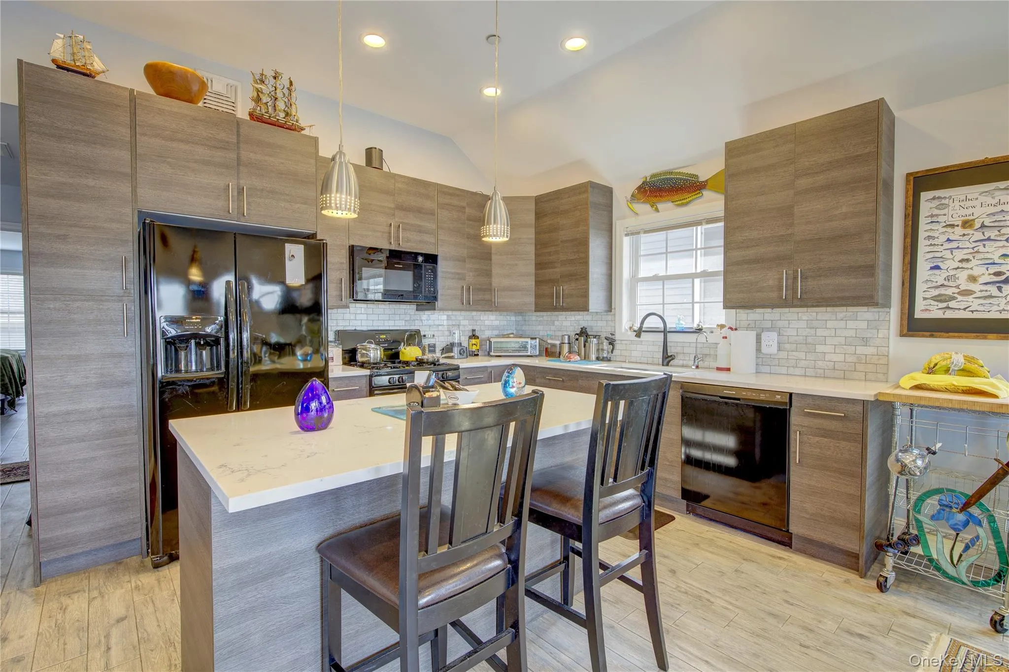 Kitchen featuring vaulted ceiling, a breakfast bar, black appliances, light wood-style floors, and pendant lighting Kitchen featuring vaulted ceiling, a breakfast bar, black appliances, light wood-style floors, and pendant lighting
