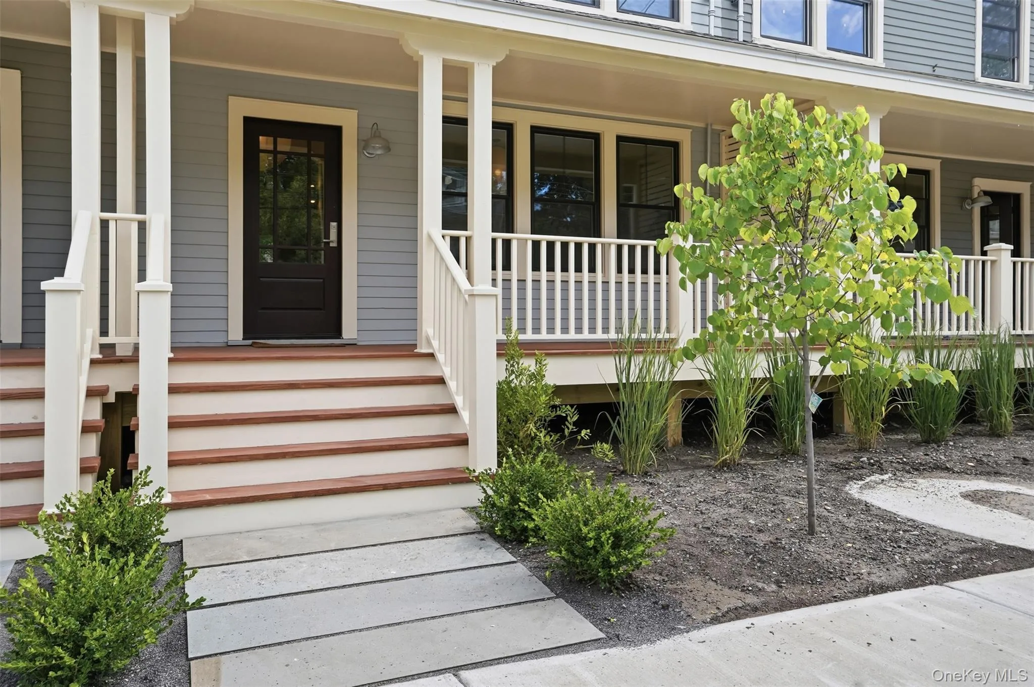 Front exterior featuring a multi-level porch, dark wood-panel door, white porch railings, and a concrete paver walkway Front exterior featuring a multi-level porch, dark wood-panel door, white porch railings, and a concrete paver walkway