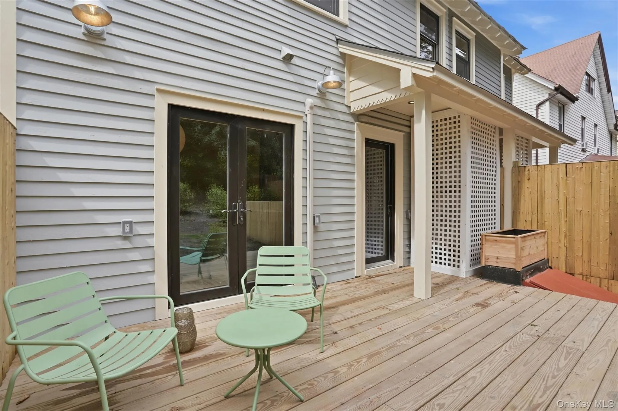 Expansive wood deck with light gray siding, privacy fencing, and dual exterior light fixtures Expansive wood deck with light gray siding, privacy fencing, and dual exterior light fixtures