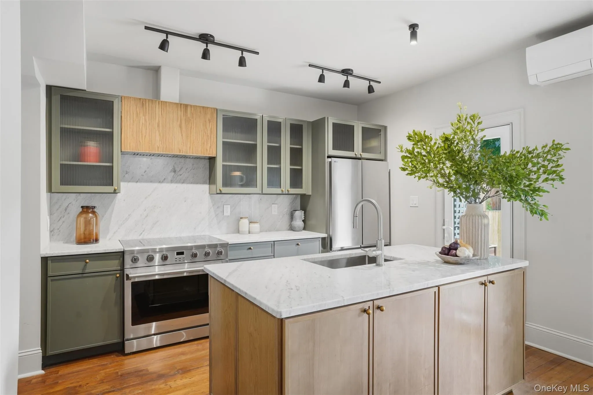 Kitchen featuring a center island, stainless steel appliances, wood-finish flooring, white countertops, and track lighting Kitchen featuring a center island, stainless steel appliances, wood-finish flooring, white countertops, and track lighting