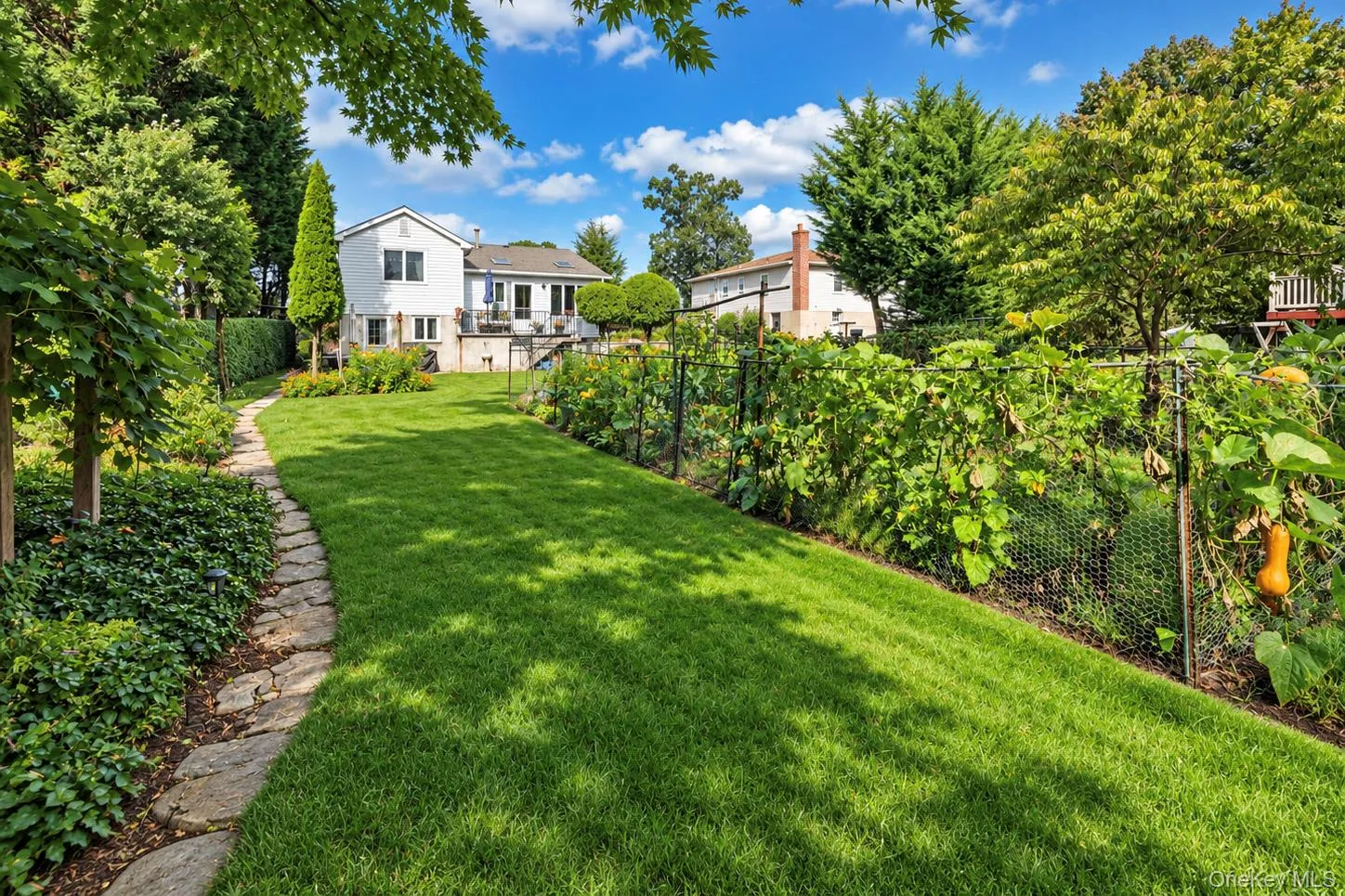Expansive backyard featuring a stone pathway, manicured lawn, established garden beds, and mature trees Expansive backyard featuring a stone pathway, manicured lawn, established garden beds, and mature trees
