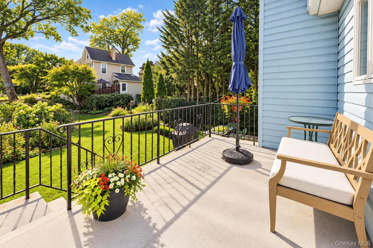 Concrete patio with black wrought iron railing, blue horizontal siding, and a white-framed window Concrete patio with black wrought iron railing, blue horizontal siding, and a white-framed window