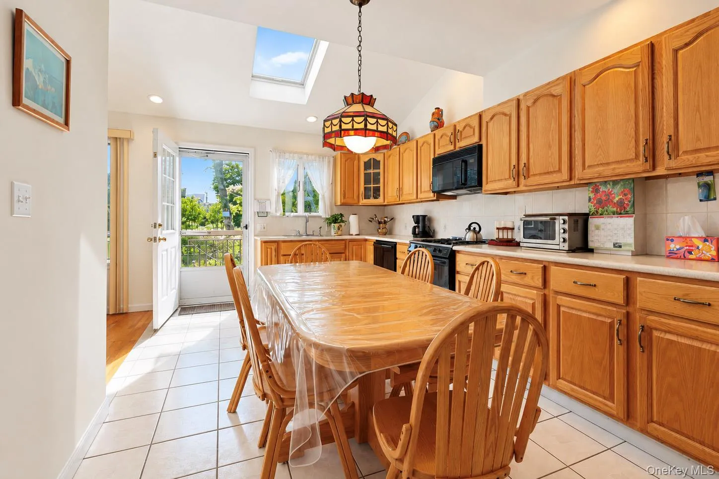 Kitchen featuring a vaulted ceiling with skylight, white tile flooring, wood-finish cabinetry, and a door with glass panels Kitchen featuring a vaulted ceiling with skylight, white tile flooring, wood-finish cabinetry, and a door with glass panels