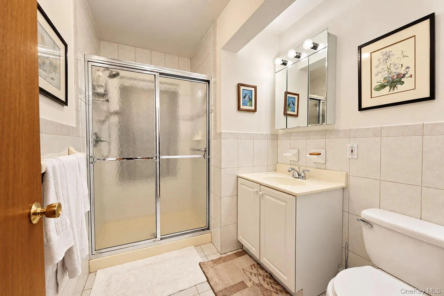 Tiled shower enclosure with sliding glass doors, single vanity with integrated sink, dual-door mirrored medicine cabinet, and wall-mounted lighting fixture Tiled shower enclosure with sliding glass doors, single vanity with integrated sink, dual-door mirrored medicine cabinet, and wall-mounted lighting fixture