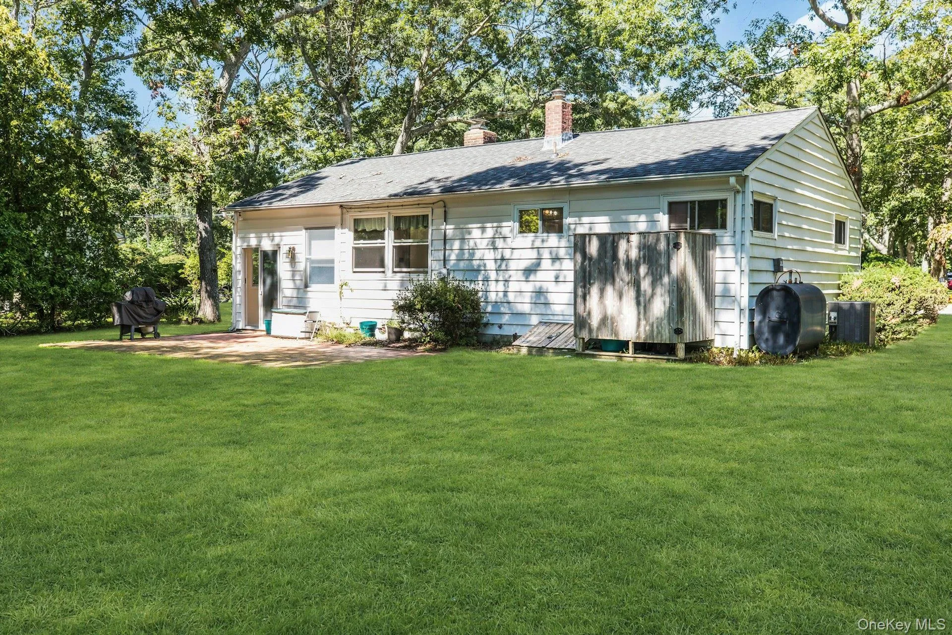 Expansive manicured lawn, mature trees, white siding exterior, shingle roof, and a brick chimney Expansive manicured lawn, mature trees, white siding exterior, shingle roof, and a brick chimney