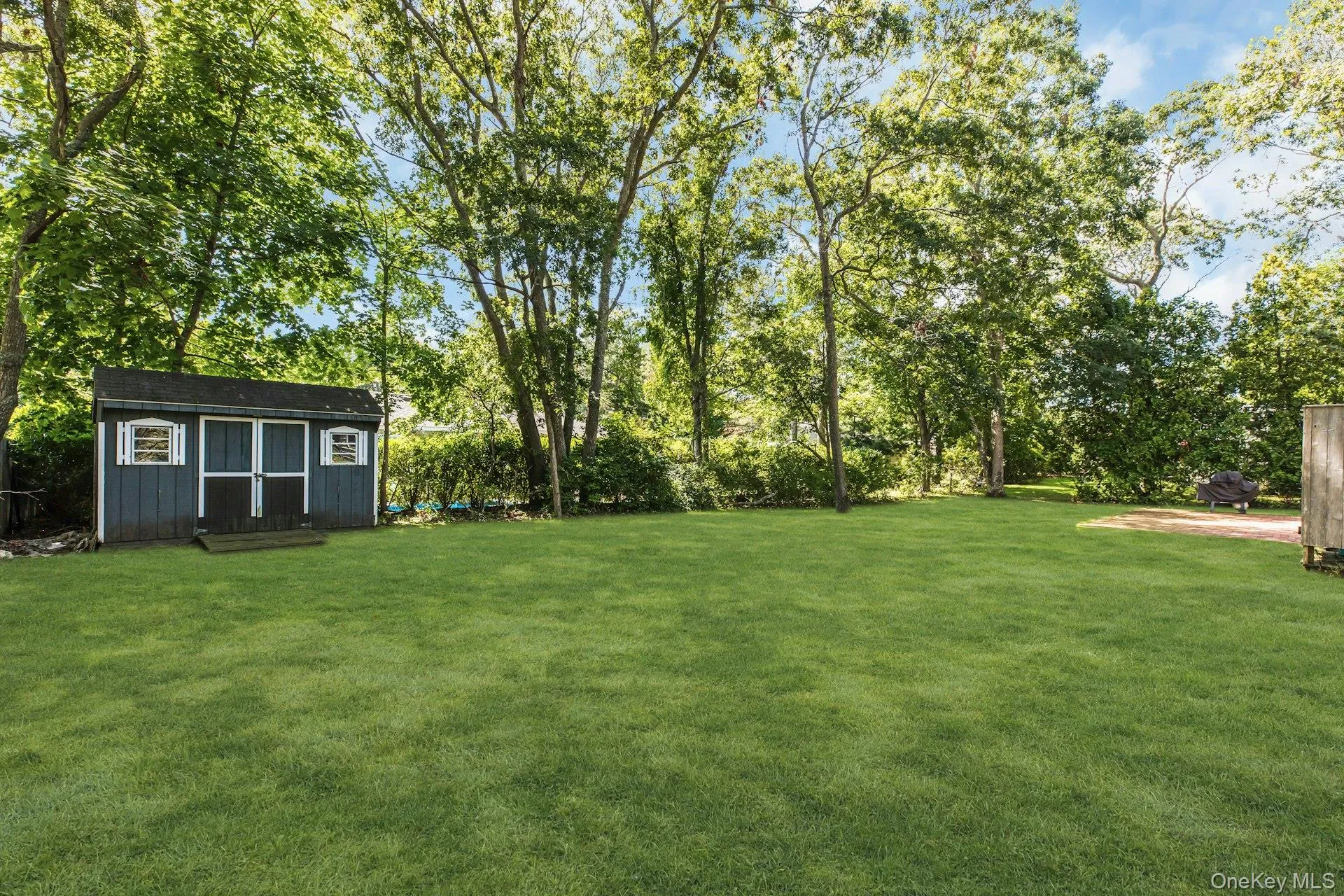 Expansive lawn with mature trees, a detached storage shed featuring double doors, and a gravel area Expansive lawn with mature trees, a detached storage shed featuring double doors, and a gravel area