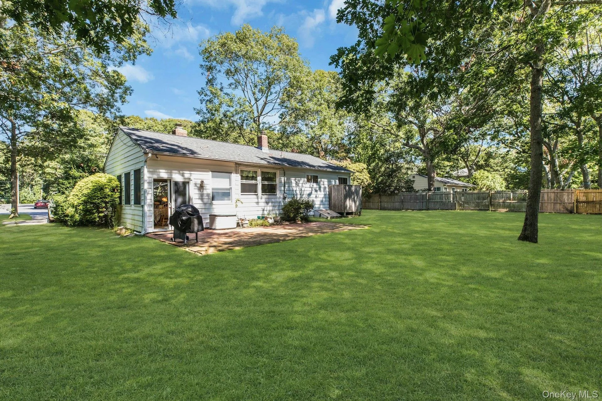 Expansive green lawn, mature trees, white siding exterior, brick patio, and a privacy fence Expansive green lawn, mature trees, white siding exterior, brick patio, and a privacy fence