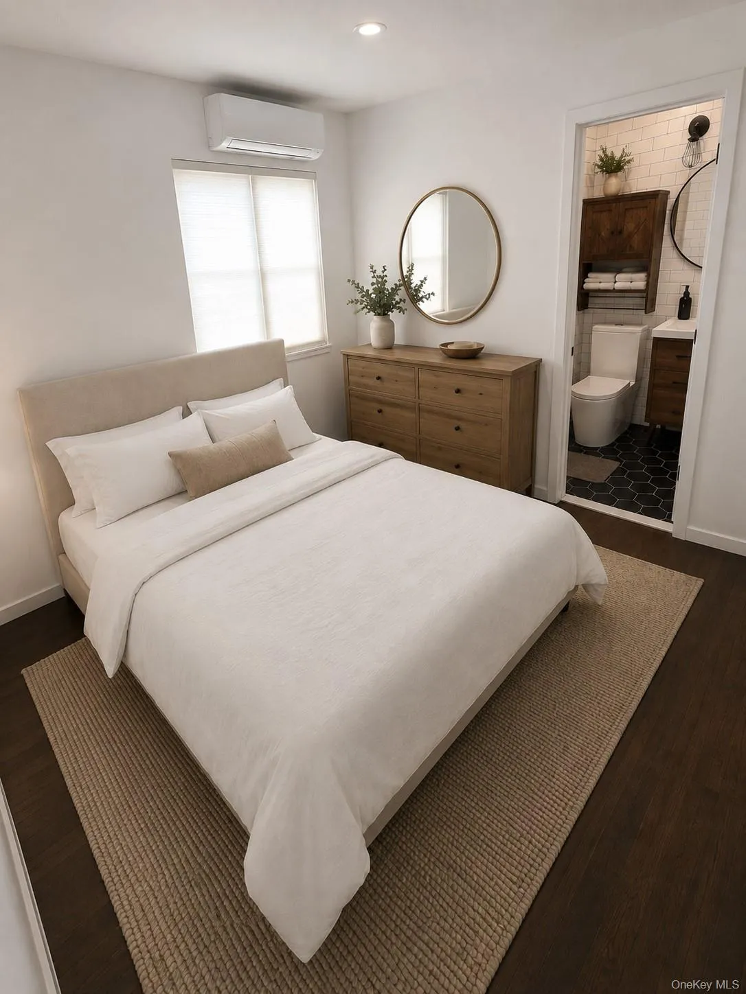Dark wood-finish flooring with recessed lighting, an integrated wall-mounted air conditioning unit, and an adjoining bathroom featuring hexagonal floor tiles and white subway wall tiles Dark wood-finish flooring with recessed lighting, an integrated wall-mounted air conditioning unit, and an adjoining bathroom featuring hexagonal floor tiles and white subway wall tiles