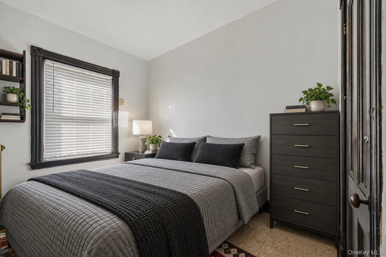 Virtually Staged Furniture. Cozy bedroom with a large window, original dark trim, neutral walls, and natural light Virtually Staged Furniture. Cozy bedroom with a large window, original dark trim, neutral walls, and natural light