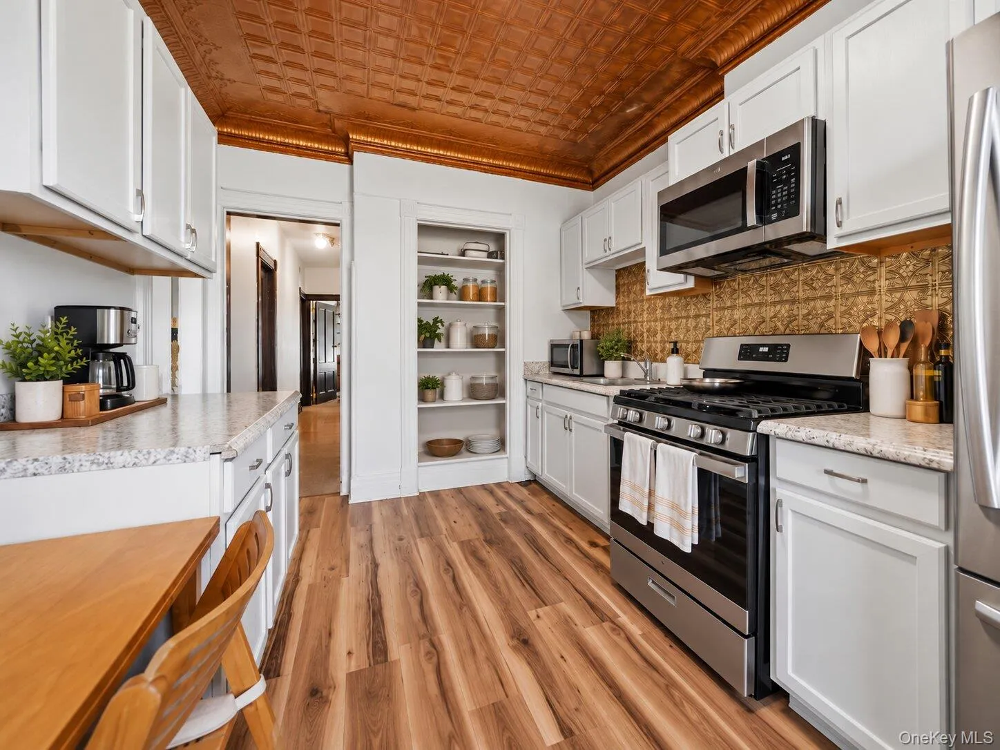 Virtually Staged Furniture. Spacious kitchen with white cabinetry, stainless steel appliances, gas range, decorative backsplash, wood-look flooring, and copper-toned patterned ceiling. Virtually Staged Furniture. Spacious kitchen with white cabinetry, stainless steel appliances, gas range, decorative backsplash, wood-look flooring, and copper-toned patterned ceiling.