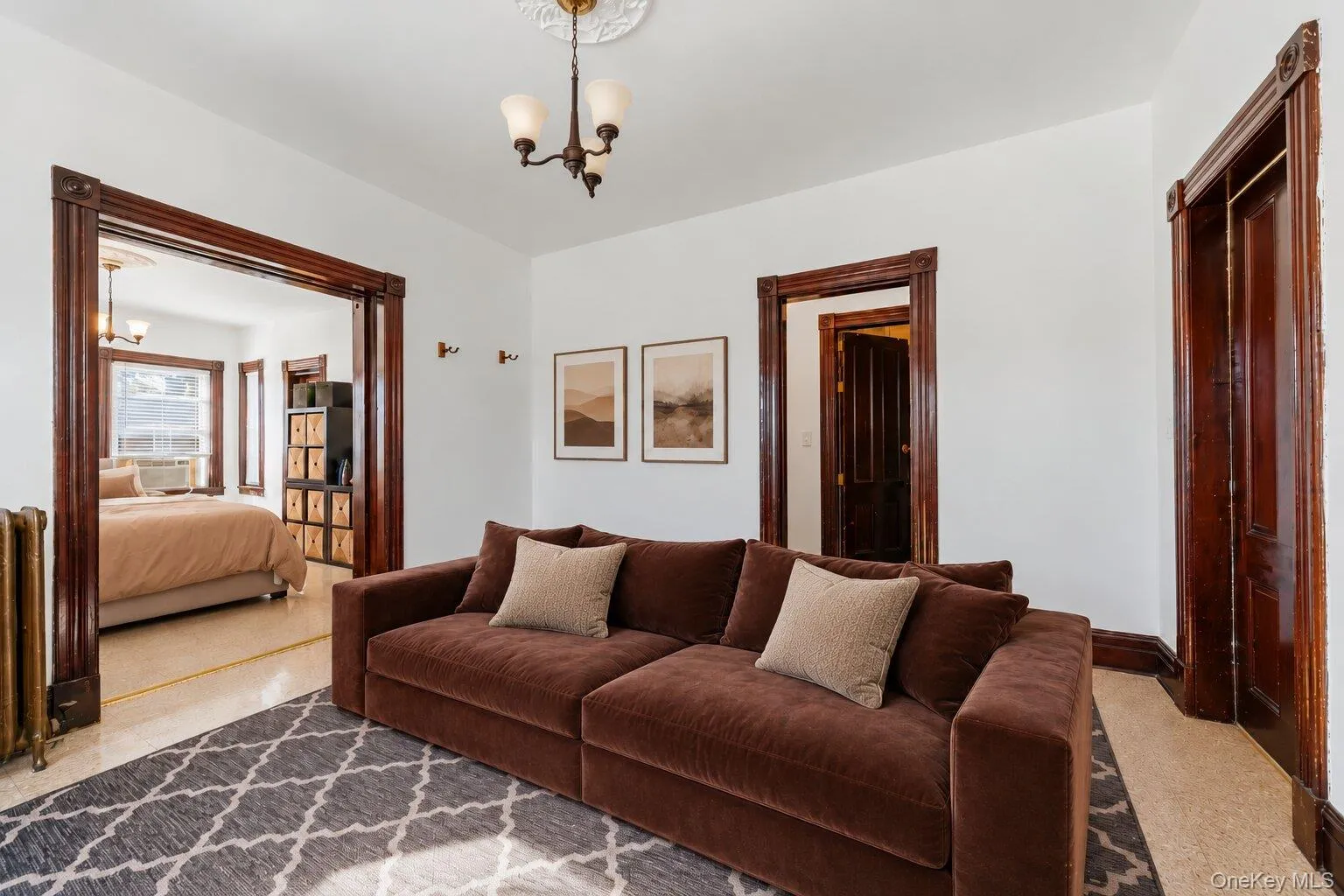 Virtually Staged Furniture. Living room with multiple windows, radiator, dark wood trim, and an adjoining bedroom visible through the doorway. Virtually Staged Furniture. Living room with multiple windows, radiator, dark wood trim, and an adjoining bedroom visible through the doorway.