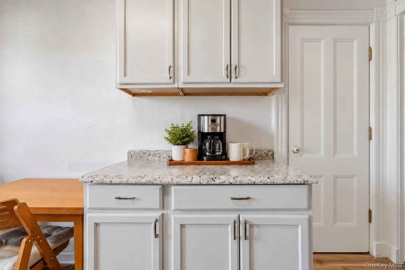 Virtually Staged Furniture. Additional kitchen counter area with white cabinetry, stone-look countertop, coffee station, adjacent dining table, and traditional interior door. Virtually Staged Furniture. Additional kitchen counter area with white cabinetry, stone-look countertop, coffee station, adjacent dining table, and traditional interior door.
