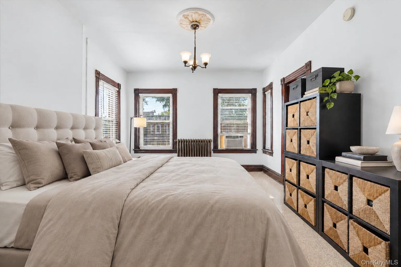 Virtually Staged Furniture. Spacious bedroom highlighting multiple windows, original wood trim, radiator, and wall-mounted Virtually Staged Furniture. Spacious bedroom highlighting multiple windows, original wood trim, radiator, and wall-mounted