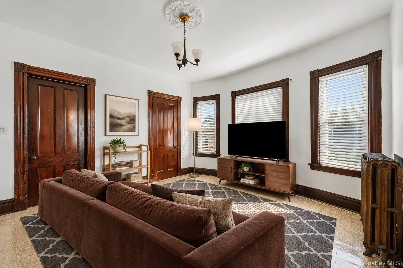 Virtually Staged Furniture. Living area with multiple windows, radiator, and original dark wood trim. Virtually Staged Furniture. Living area with multiple windows, radiator, and original dark wood trim.