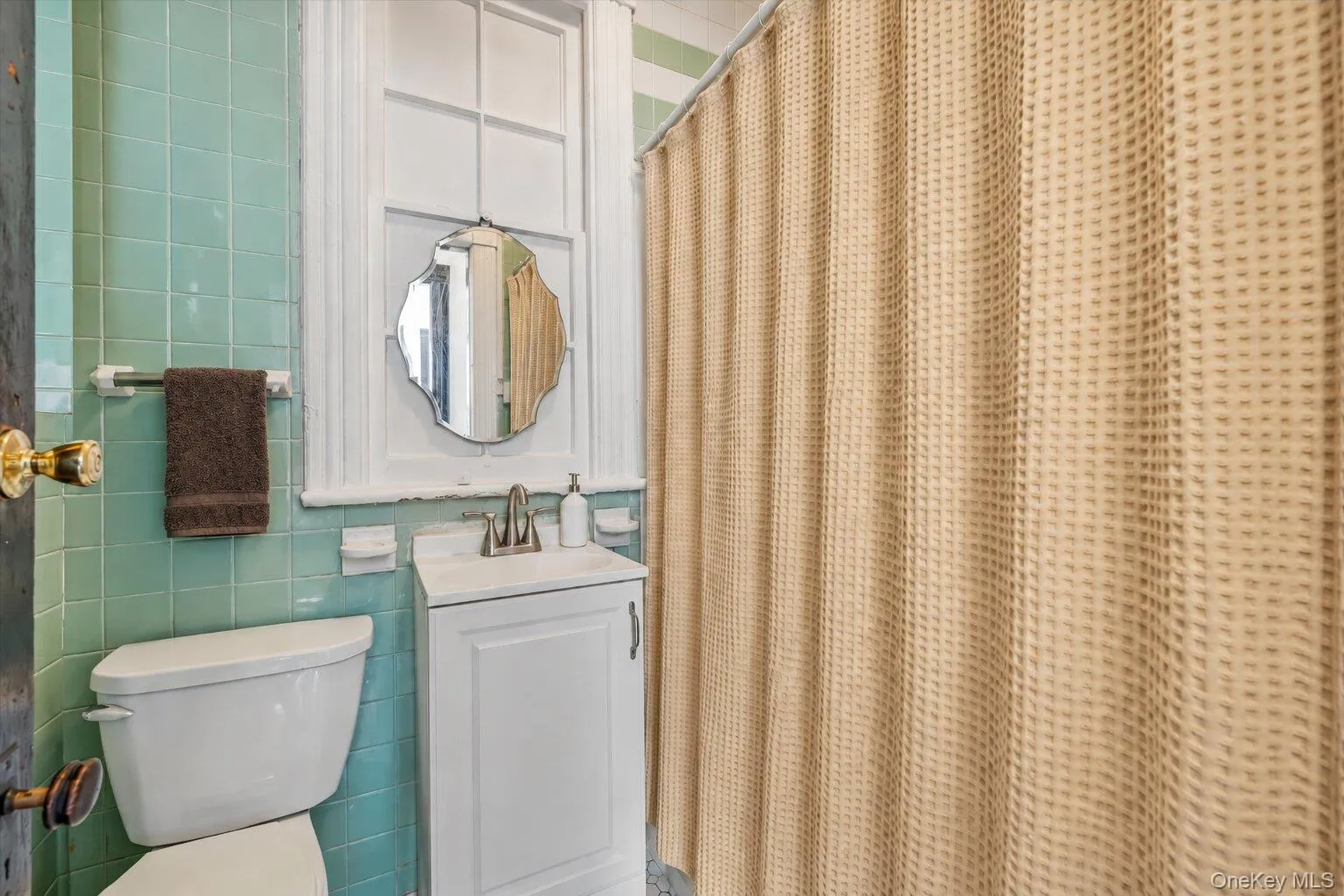 Bathroom featuring aqua tile walls, white vanity, toilet, mirror, and tub/shower area. Bathroom featuring aqua tile walls, white vanity, toilet, mirror, and tub/shower area.
