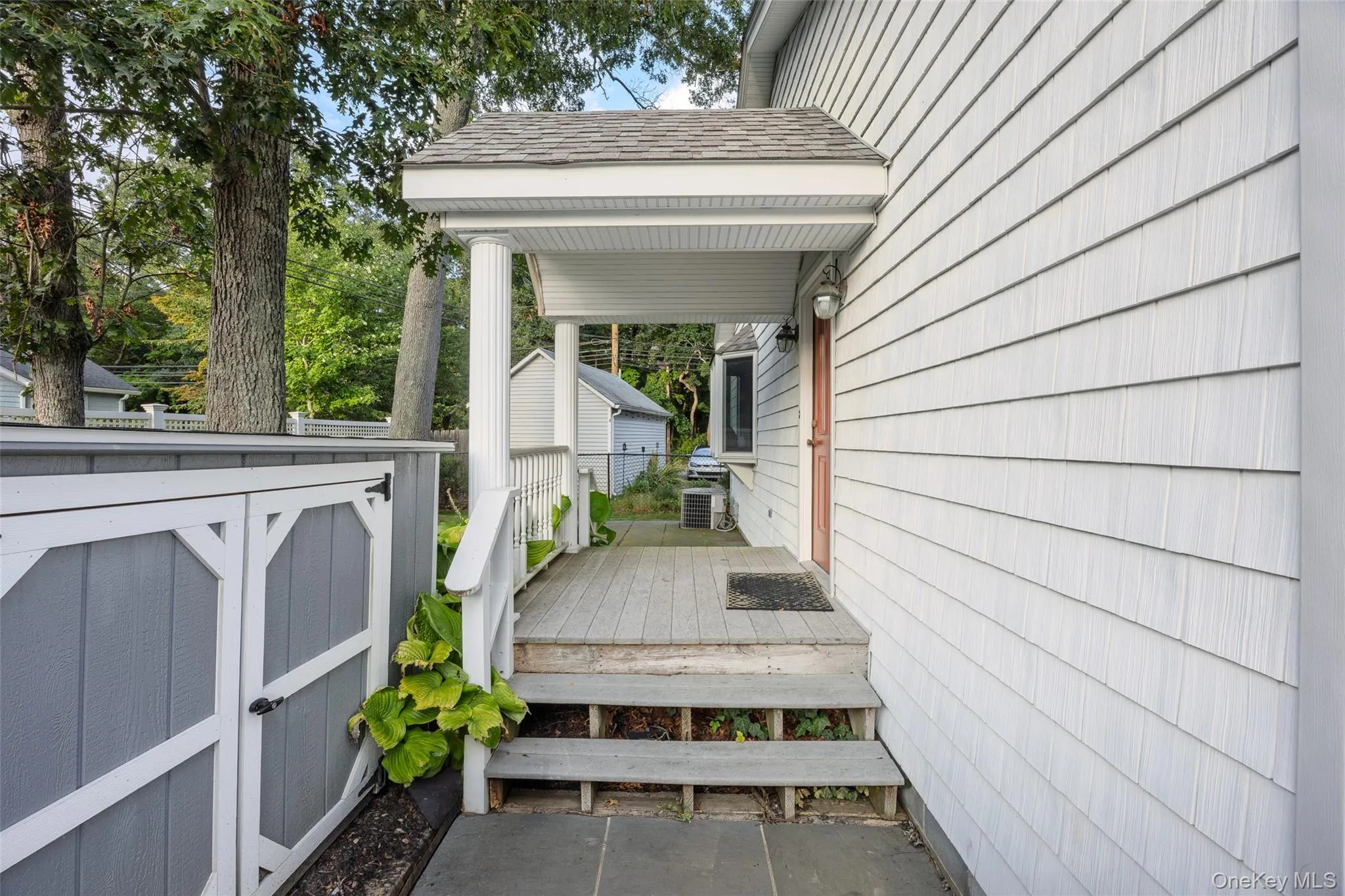 Covered porch with wood decking and white railing, leading to a paneled entry door Covered porch with wood decking and white railing, leading to a paneled entry door