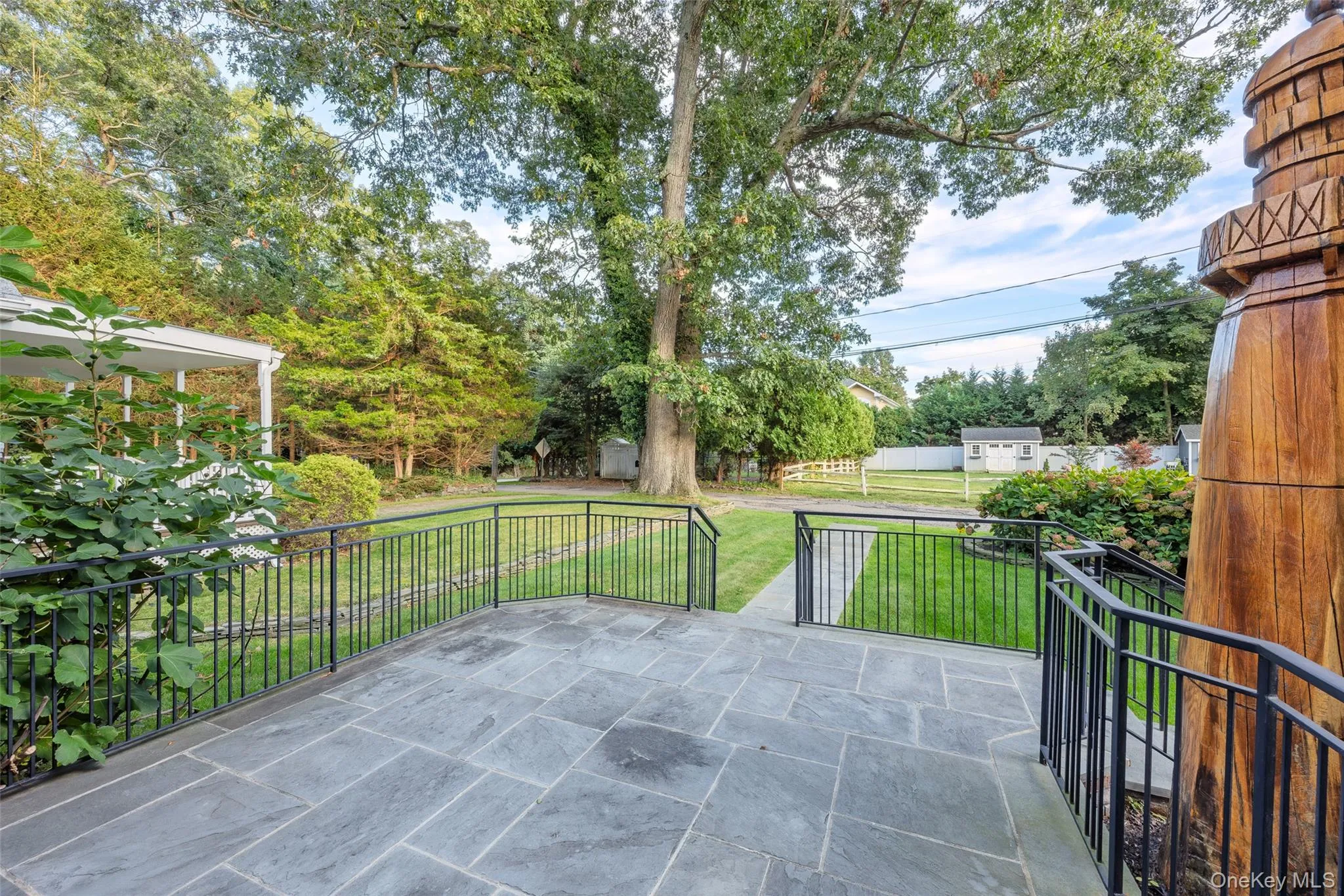 Stone patio with black iron railings, a manicured lawn, and mature trees Stone patio with black iron railings, a manicured lawn, and mature trees
