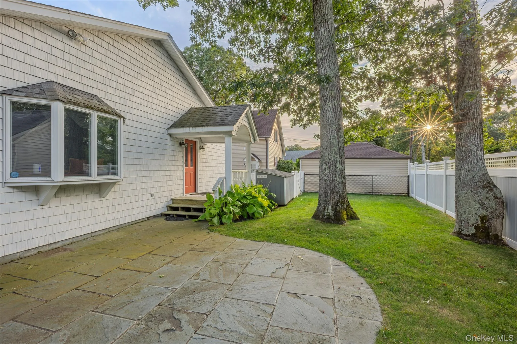 Stone patio with a curved edge, shingle siding, a bay window, and a covered entry Stone patio with a curved edge, shingle siding, a bay window, and a covered entry