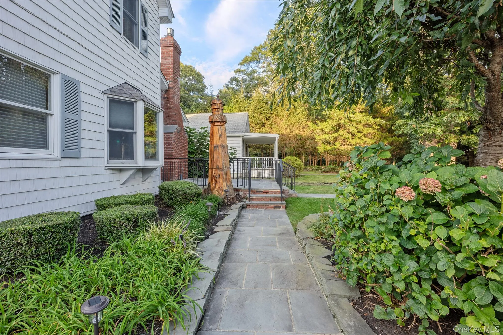 Shingle siding exterior with a bay window, brick chimney, stone paver walkway, and mature landscaping Shingle siding exterior with a bay window, brick chimney, stone paver walkway, and mature landscaping