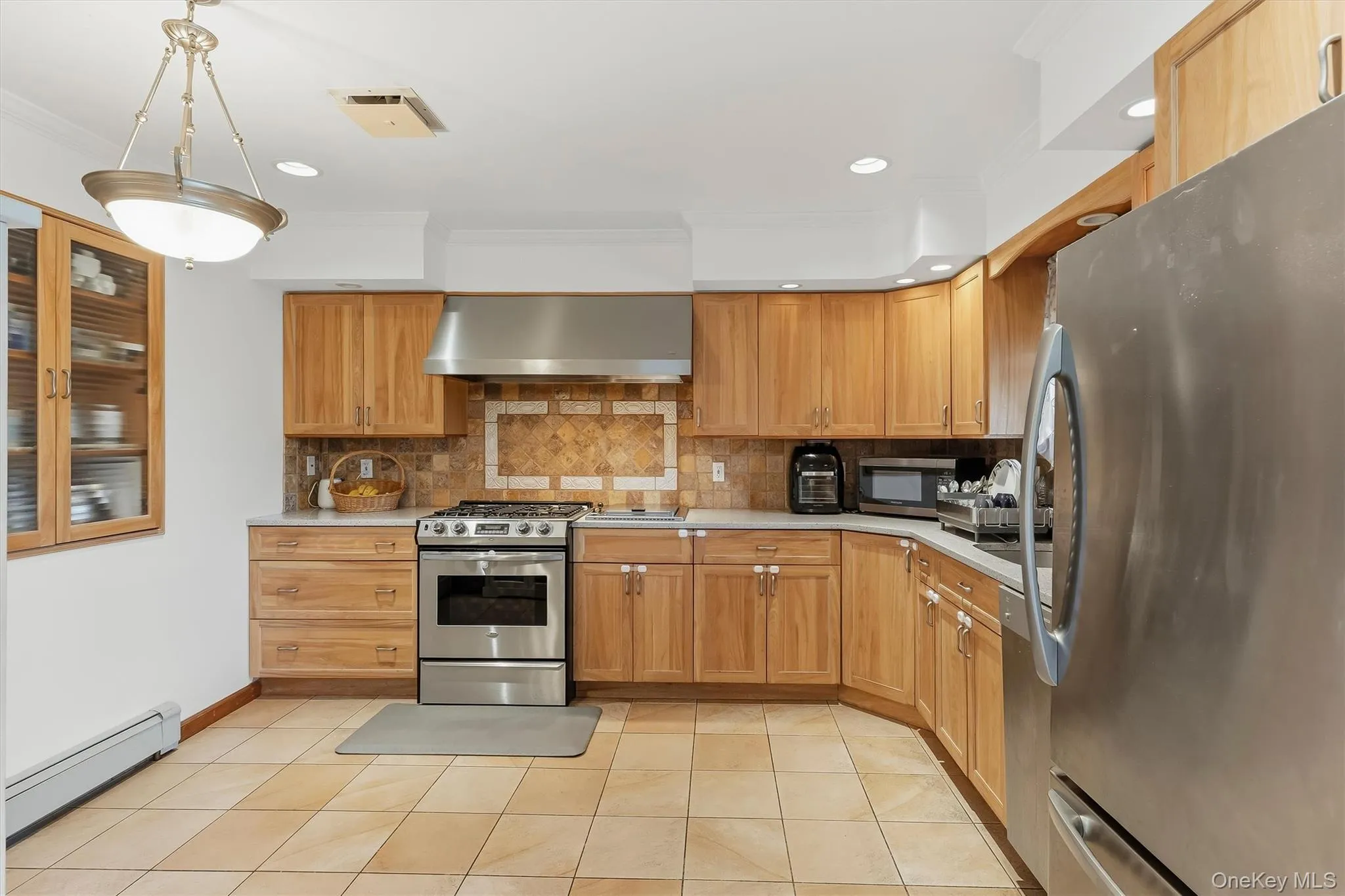 Kitchen featuring wood cabinetry, stainless steel appliances, tile flooring, and a decorative tile backsplash Kitchen featuring wood cabinetry, stainless steel appliances, tile flooring, and a decorative tile backsplash