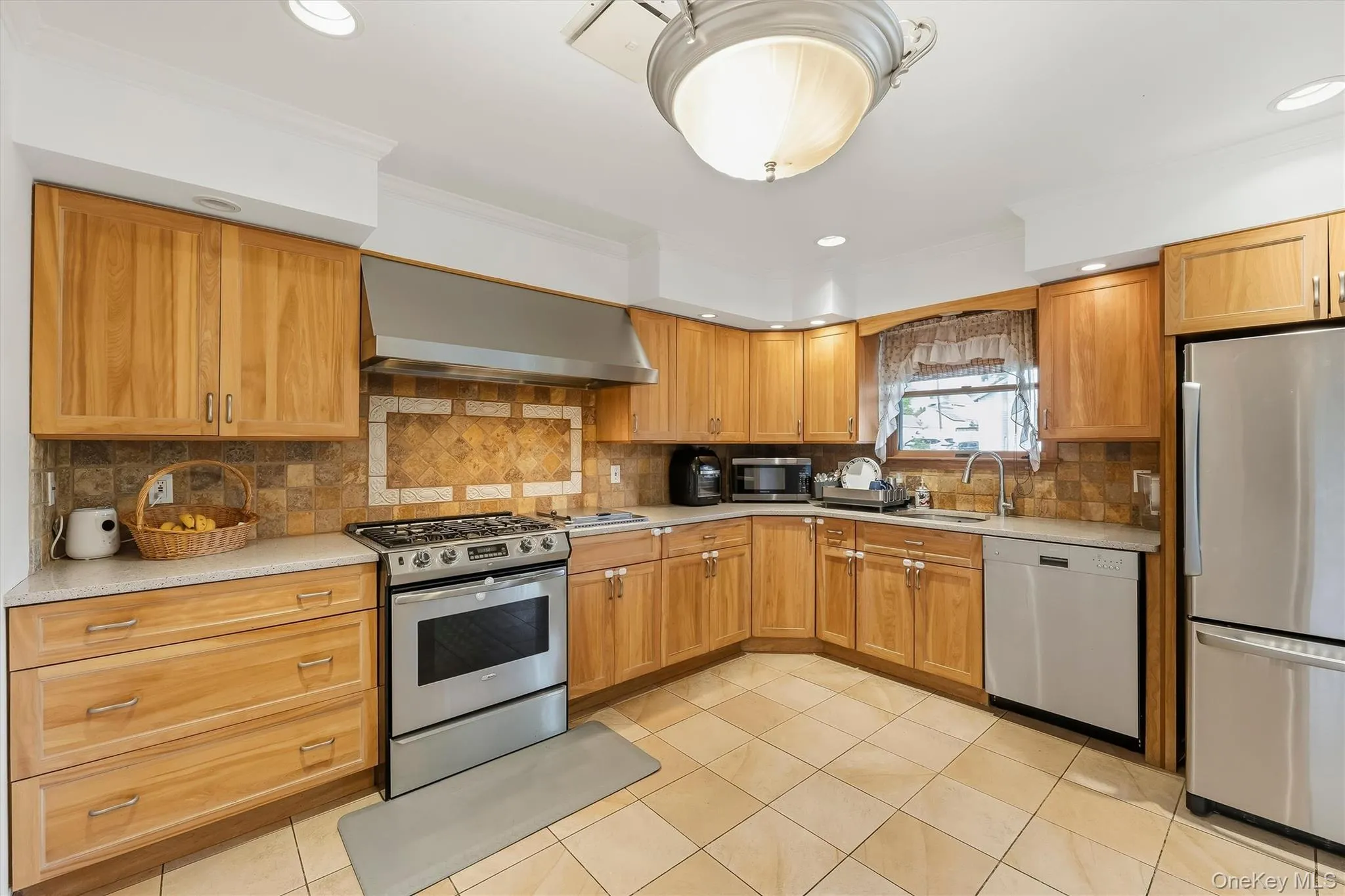 Kitchen featuring wood-finish cabinetry, tile flooring, stainless steel appliances, and a tile backsplash Kitchen featuring wood-finish cabinetry, tile flooring, stainless steel appliances, and a tile backsplash